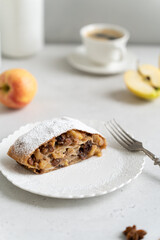 Apple pie - strudel or Apfelstrudel, sliced pie with apples, raisin and cinnamon on a white table. Traditional German or Austrian pastry. Homemade apple strudel with fresh apples and powdered sugar.
