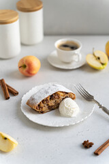 Apple pie - strudel or Apfelstrudel, sliced pie with apples, raisin, cinnamon and ice cream on white plate. Traditional German Austrian pastry. Homemade strudel with fresh apples and powdered sugar