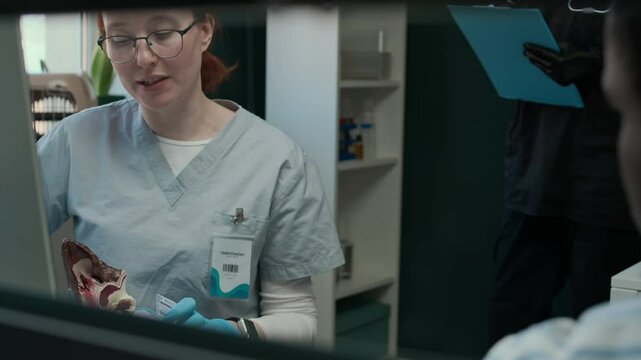 Caucasian female vet showing pet owner how to give ear drops while using anatomy auricle layout during consultation in modern clinic