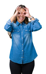 Young beautiful brunette woman wearing blue denim shirt over isolated background doing ok gesture like binoculars sticking tongue out, eyes looking through fingers. Crazy expression.