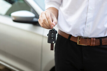 A man holds a car key with anticipation, the gleaming metal reflecting his excitement. In the background, the sleek silhouette of the car sets the stage for a journey filled with possibilities