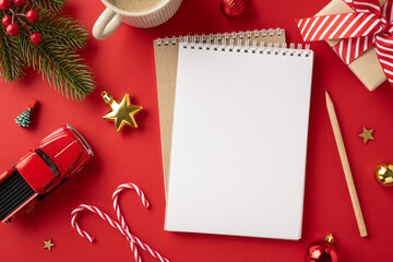 Top view of a Christmas-themed desk with a blank notebook, ornaments, and festive decorations on a red background