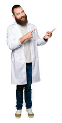 Young blond scientist man wearing white coat smiling and looking at the camera pointing with two...