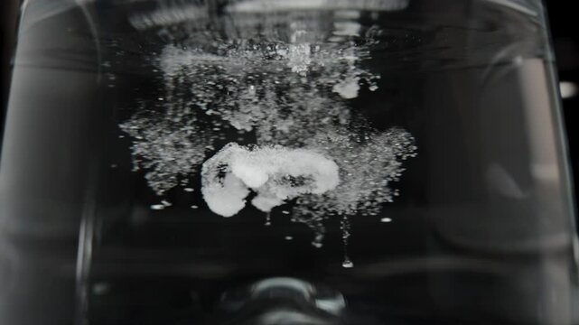 Close-up of Creatine powder dissolving in water, forming clumps as it begins to mix for better absorption. Slow motion.