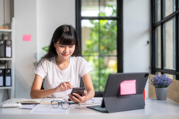 Fototapeta premium Young asian accountant woman smiling and calculating finances using calculator and smartphone