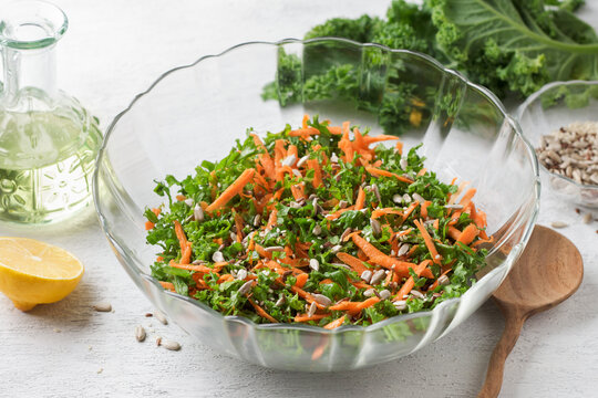 Chopped kale leaves with carrots in a transparent salad bowl on a light gray background
