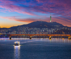 Seoul City after sunset and a sightseeing boat on the Han River and a bridge with Namsan Mountain and Seoul Tower in the background, Seoul, South Korea.
