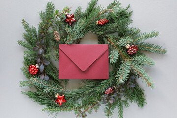 Overhead view of an envelope in the middle of a coniferous festive Christmas wreath decorated with christmas baubles on a grey background