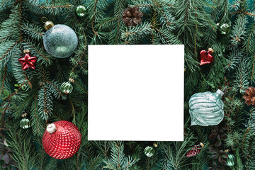 Close-up of a Blank piece of card on a background of Assorted coniferous branches decorated with festive Christmas baubles