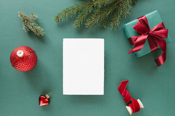 Overhead view of a blank piece of deckle edge card  with a wrapped Christmas gift and assorted Christmas decorations on a green background