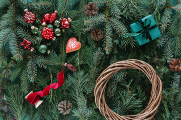Overhead view of a wrapped gift, wicker wreath, pine cones and assorted Christmas baubles on a background of Assorted coniferous branches decorated with festive Christmas baubles