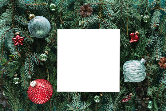 Close-up of a Blank piece of card on a background of Assorted coniferous branches decorated with festive Christmas baubles