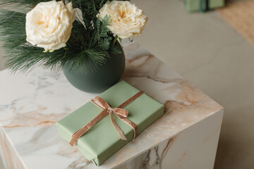 Overhead view of a Vase of white roses and conifer branches on a table net to a wrapped Christmas gift