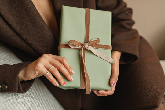 Close-up of an elegant well dressed woman sitting on a sofa holding a wrapped gift box