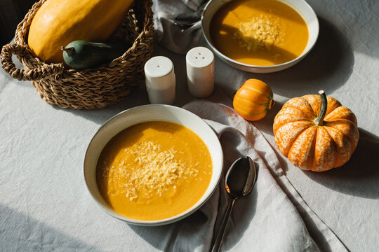Overhead view of two bowls of homemade pumpkin soup with Parmesan on a table with fresh pumpkins