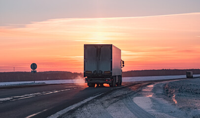 Semi truck driving along a snowy highway at sunset in winter