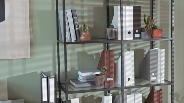 No people tilt shot of open shelf with multiple folders, books and small cacti in pots in modern office with olive walls