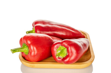 Three sweet red peppers on a bamboo plate, macro, isolated on white background.