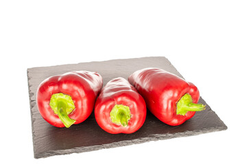 Three sweet red peppers on slate stone, macro, isolated on white background.