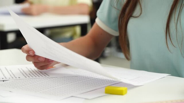 High school teenagers in classroom, close up shot girl at desk writing exam on paper, doing math task. Modern education concept.