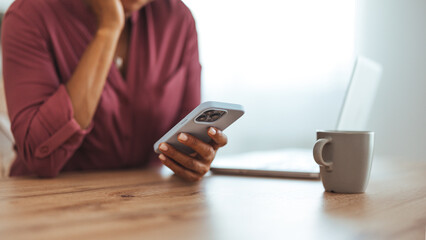 Woman Using Smartphone at Home with Laptop and Coffee