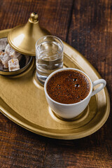 Turkish coffee in classic coffee cup with water and Turkish delight on wooden table