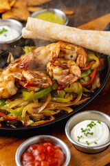 Shrimp fajitas on wooden table with sauces and tortillas on the side