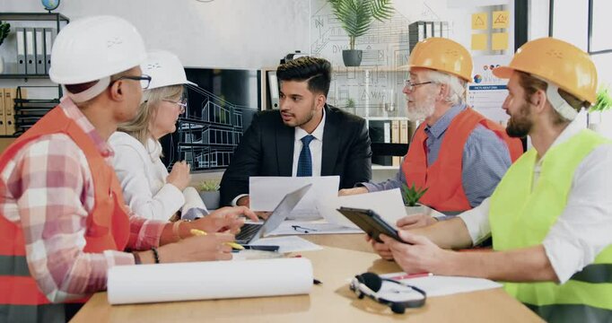 Man main engineer discussing working questions together with professional diverse man and woman team of engineers in meeting room