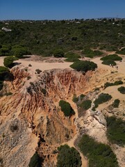The photo shows the impressive limestone arches near Benagil Cave in the Algarve, Portugal. Crystal-clear green waters flow beneath the towering cliffs, set against a bright blue sky and rugged coastl