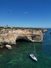 The photo shows the impressive limestone arches near Benagil Cave in the Algarve, Portugal. Crystal-clear green waters flow beneath the towering cliffs, set against a bright blue sky and coastline.