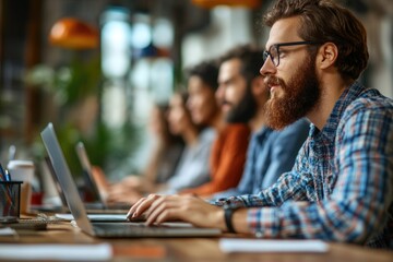 Fototapeta premium A man with a beard is typing on a laptop in front of a group of people