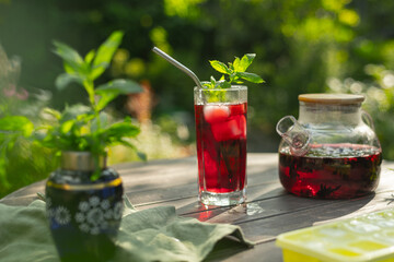 Iced red hibiscus tea with mint. Summer cocktail on wooden table outdoors