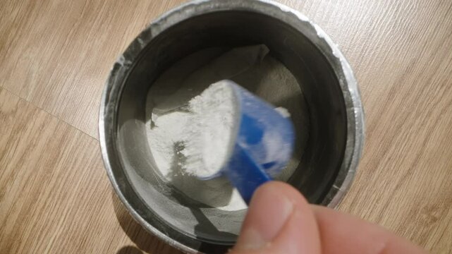 Reaching into the pre-workout powder jar with a blue scoop, preparing to measure a serving. Dolly slider, close up. Slow motion.