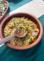 Bulgur cooked with green pepper, onion and parsley in a ceramic bowl on the table during dinner. Homemade dishes. The concept of traditional Turkish cuisine. Vertical orientation.