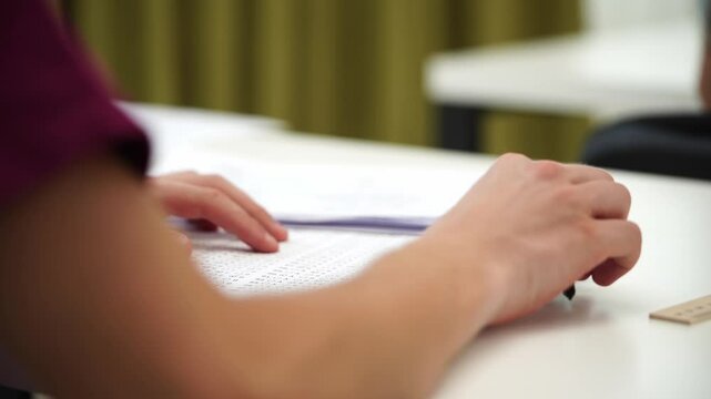 High school teenagers in classroom, boy writing exam using smartphone to check right answers, writing from cheat sheet. Modern education concept.