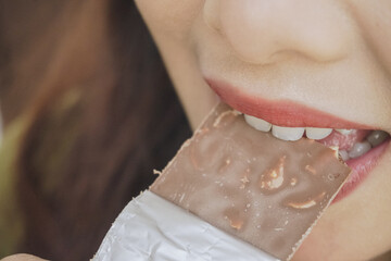 Close up portrait of Asian woman eating a chocolate bar while smiling as she enjoys her snack.