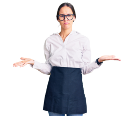 Beautiful brunette young woman wearing professional waitress apron clueless and confused with open arms, no idea concept.