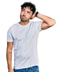 Fototapeta premium Hispanic young man with beard wearing casual white t shirt confuse and wondering about question. uncertain with doubt, thinking with hand on head. pensive concept.