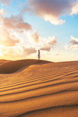 young man in a traditional Abaya outfit stands in the stunning desert with undulating texture and...