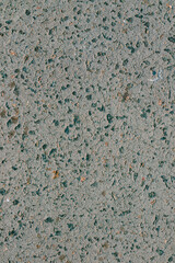 Close-up of a rough concrete surface with variously sized stones and gravel embedded, showing a textured gray pattern with blue and orange inclusions.
