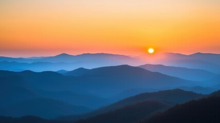 Obraz premium A serene sunset over misty mountains, showcasing layers of blue and orange hues that inspire tranquility and natural beauty.