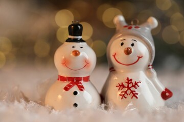 Funny snowman figures on artificial snow against blurred lights, closeup