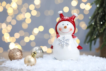 Funny snowman figure and Christmas balls on artificial snow against blurred lights