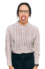 Fototapeta premium Young hispanic girl wearing casual clothes and glasses sticking tongue out happy with funny expression. emotion concept.