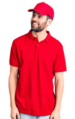 Young handsome man with beard wearing delivery uniform looking away to side with smile on face, natural expression. laughing confident.