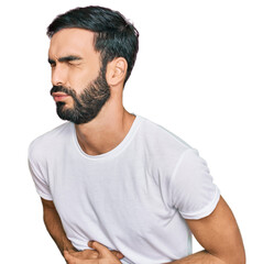 Young hispanic man wearing casual white t shirt with hand on stomach because nausea, painful disease feeling unwell. ache concept.