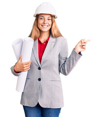 Beautiful young woman wearing architect hardhat holding build project smiling happy pointing with...