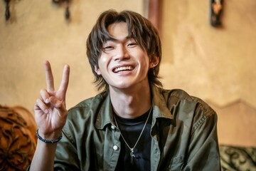 Happy young man peace sign. A joyful young man with a relaxed expression, wearing a green jacket and a silver necklace, makes a peace sign.