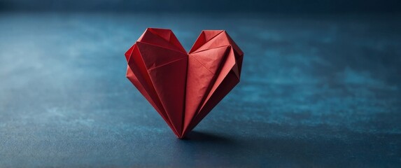 Red paper heart folded into origami shape on blue background.