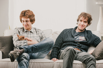 Two male roommates relaxing on sofa with dog